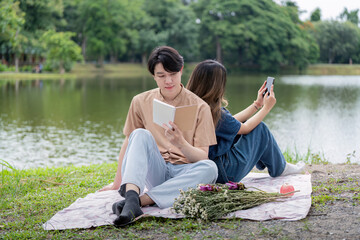 Asian young couple enjoying picnic reading by tranquil lakeside