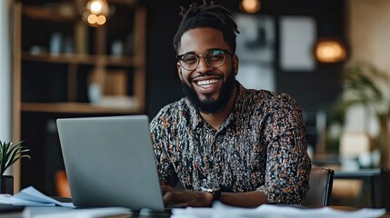 A professional entrepreneur man sitting in front of a laptop, smiling at the screen, with papers and notes scattered on the desk.