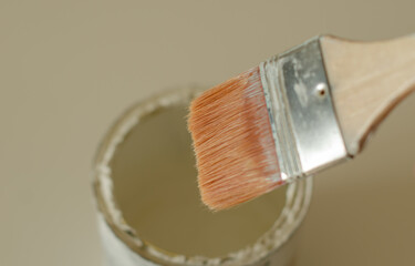 Close-up of a paintbrush above a white paint can, focusing on the bristles and handle. The image...