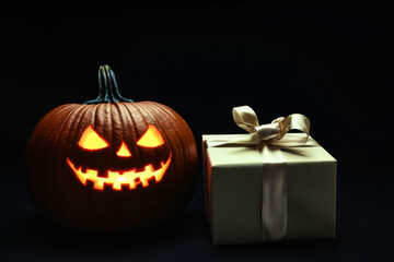 A Carved Pumpkin With a Glowing Face and a Wrapped Gift
