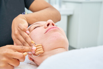 beautician performing a facial wood therapy treatment on a woman with a striated roller
