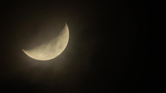 Waxing crescent in the dark night sky with flying clouds. Crescent Moon shooting through a telephoto lens, close-up. Free space for text