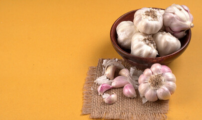 Organic Garlic. Fresh Garlic Cloves and Garlic bulb in wooden basket on yellow background with Pile of garlic or spice. Concept of spices for healthy cooking.