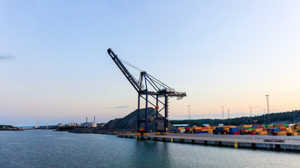 Fototapeta premium Container crane at a harbor at sunset. Ideal image for themes related to global trade, industrial operations, and shipping logistics. Copy space
