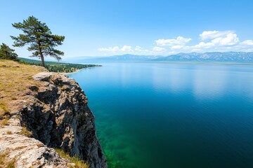 Lone tree on a cliff overlooking a vast blue lake.