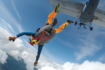 Skydiving tandem jumping out of a plane above the clouds