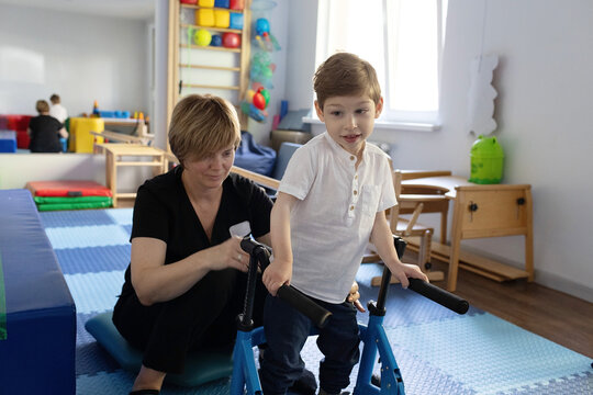 Young boy with cerebral palsy practices using a walker with guidance from his physical therapist in room for physical therapy