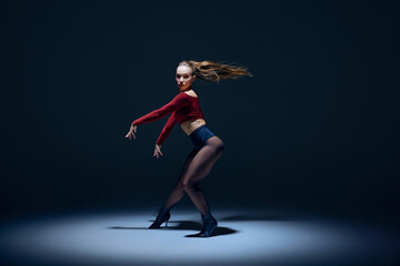 Talented, artist and sensual young woman performing dynamic high heels dance against dark studio...