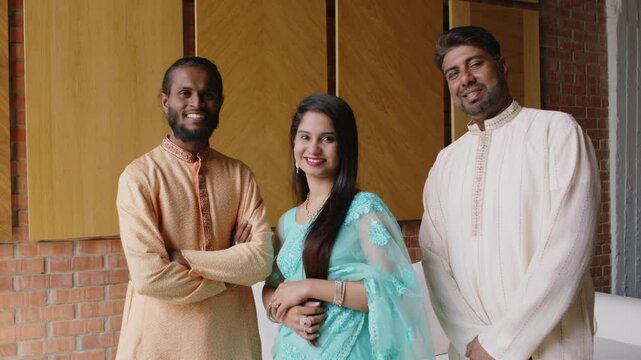 Group portrait of two Indian male colleagues dressed in kurta and young female coworker standing between them in saree smiling and looking at camera