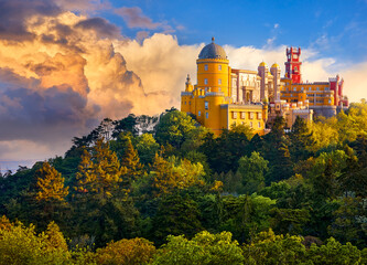 Sintra, Portugal. Palace of Pena in the National park. Lisbon. Sunrise among green trees. Beautiful fairytale castle forest pine-trees. Panoramic summer view at palace. Sunlight clouds on sky