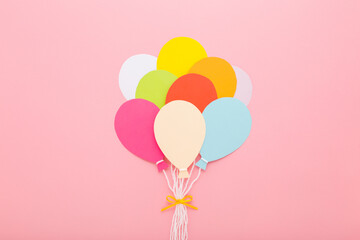 Bunch of colorful balloon shapes from application paper with white strings and ribbon on light pink table background. Pastel color. Closeup. Top down view.