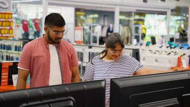 Indian couple choosing new plasma tv in home appliance store on Black Friday