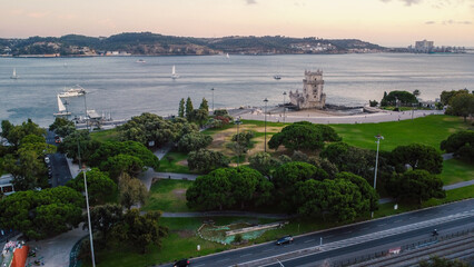 An aerial drone image of the iconic Belém Tower in Lisbon, Portugal, set against the serene backdrop of the Tagus River at sunset. Lisbon