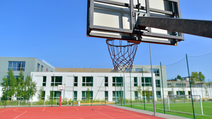 Schoolyard with basketball court and school building exterior in the sunny day. 