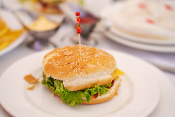 Burger of sesame buns, lettuce and cutlets with tomato sauce decorated with a skewer. fast food for a children's party.