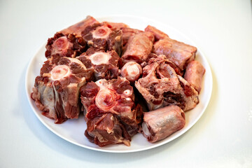 Raw beef oxtail on a round white plate in closeup.