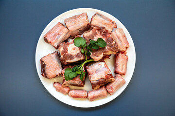 Raw beef oxtail on a round white plate in closeup.