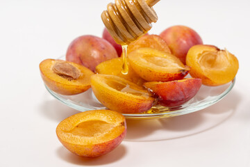 Halves of ripe sweet plums with honey on a glass plate isolated on white background.