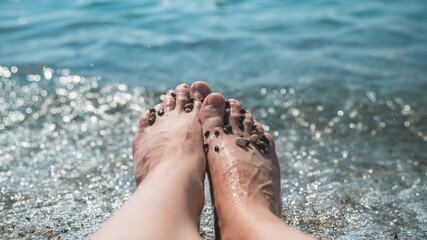close up Female feet on the background of the sea surf, on the beach with small pebbles, concept...