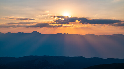 The setting sun over the mountains, the beautiful sun's rays shine through the clouds, the natural background, freedom, tranquility and peace