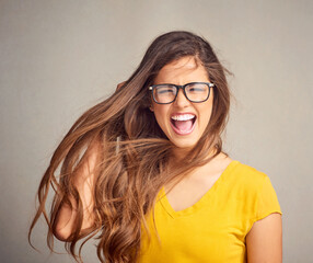 Obraz premium Happy woman, portrait and glasses with surprise for hair style or natural beauty in studio on a gray background. Young, female person or brunette model with smile, spectacles or wow for eye care