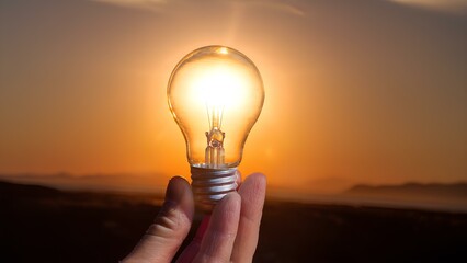 Concept: alternative energy of the Sun, crisis in the electrical system. In the hands of the bulb against the background of the setting sun.