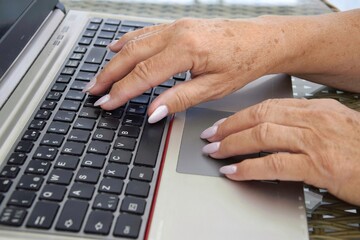 Hands of an old business woman typing on a keyboard. An elderly lady works on a laptop.