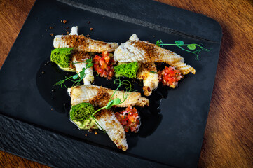 Elegant, chic dish with squid meat and vegetables on black plate. Artfully arranged, showcasing sophisticated contrast between colorful ingredients and sleek black plate. 