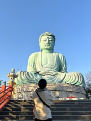 Fototapeta premium A teenage girl is standing and praying in front of the mock-up Daibutsu Buddha statue at Wat Phra That Doi Phra Chan temple, located on the serene hilltop in Mae Tha district, Lampang province of Thai