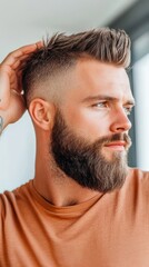 Obraz premium A man with a well-groomed beard and stylish haircut, applying pomade to his hair in front of a mirror, highlighting modern male grooming