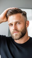 Obraz premium A man with a well-groomed beard and stylish haircut, applying pomade to his hair in front of a mirror, highlighting modern male grooming