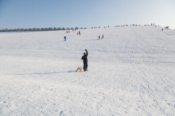 Winter landscape in Riem park, Munich, Bavaria, Germany: Young boy with a sled giving a sign with his arm for a free ride downhill