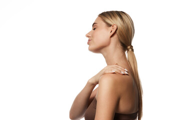 Obraz premium Portrait of attractive young woman with low ponytails doing massage of her shoulders, isolated on white studio background. Concept of skin and body care, beauty treatment, spa, wellness and health