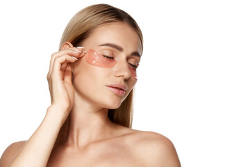 Beautiful woman with perfect clear skin, gently applying under eye patches isolated on white background. Natural beauty enhanced by effective skincare and cosmetics. Skincare routine, treatment