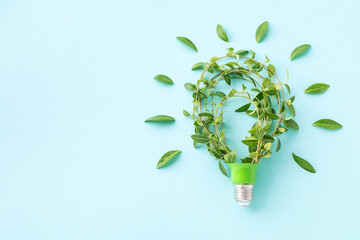 Green eco friendly lightbulb from fresh leaves on blue background top view. Energy saving, ecology...