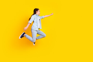 Photo of positive cute pretty girl wear trendy denim clothes fly run empty space isolated on yellow color background