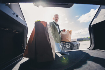 Photo of retired customer male shopping cart loading trunk car paper bags buying food mall parking...