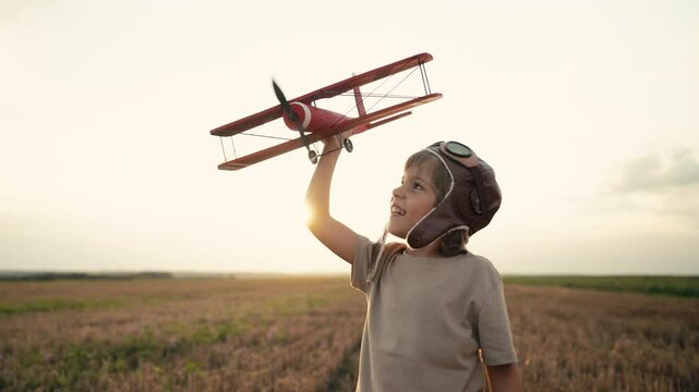 Smiling interested 5 years old child boy playing with wooden airplane, discovering future profession interest, dreamer kid flying, traveling on summer field. Creative dream, fantasy, childhood