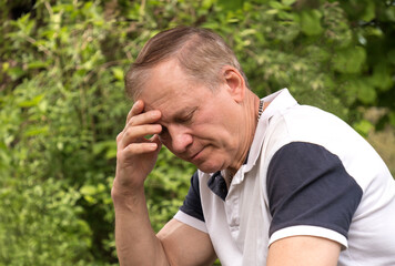 portrait of a mature man, 50-60 years old, sitting with his eyes closed in deep thought, hand on...