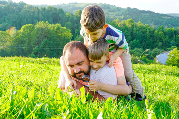 Father and sons exploring nature, looking at plants insects though magnifying glass