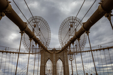 Obraz premium Iconic Bridge with Dramatic Sky. Photo of a famous bridge with towering archways and steel cables set against a cloudy, dramatic sky captured during daytime.