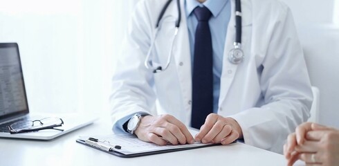 Doctor and a patient. The physician, wearing a white medical coat over a blue shirt and tie, gesturing with his hands during a consultation in the clinic. Medicine concept