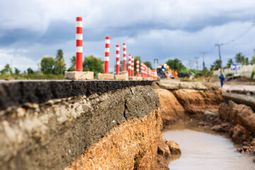 An asphalt road is severely damaged by erosion and flooding, clearly exposing the layers of rock...
