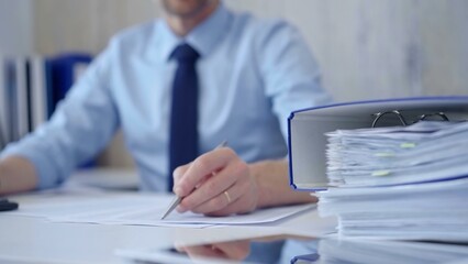 Unknown man accountant with blue t-shirt concentrating while calculating costs and taking notes at his desk. Taxes, audit in business