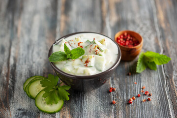 Indian Fresh sauce called Raita with herbs, dahi and sliced cucumber in a bowl on the table.