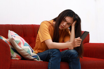 Bad news on device screen. Upset asian woman frustrated by problem with work or relationships, sitting on couch, feeling despair and anxiety, loneliness, having psychological trouble