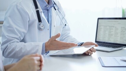 Doctor and a patient. The physician, wearing a white medical coat over a blue shirt, is using tablet computer during a consultation in the clinic. Medicine and science