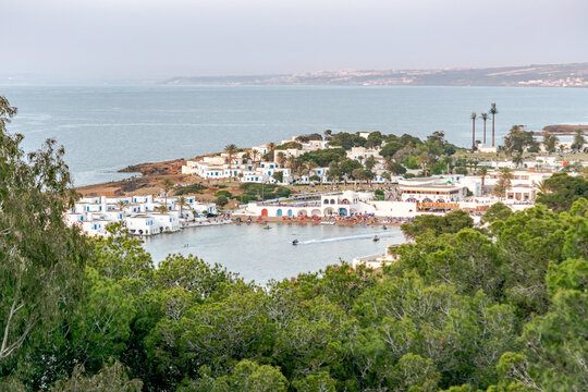 Tourist complex CET beach of Tipaza. Elevated view with trees frame showing unrecognizable people enjoying the sun and summer with aquatic activities like jet-skiing, pedal-boating, and kayaking.
