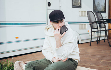 Young Caucasian man sitting and holding the phone outside the motor house.