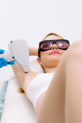 A young woman relaxes on a sofa in a salon during a laser hair removal procedure. Perfect for showcasing comfortable care and cutting-edge cosmetology techniques.